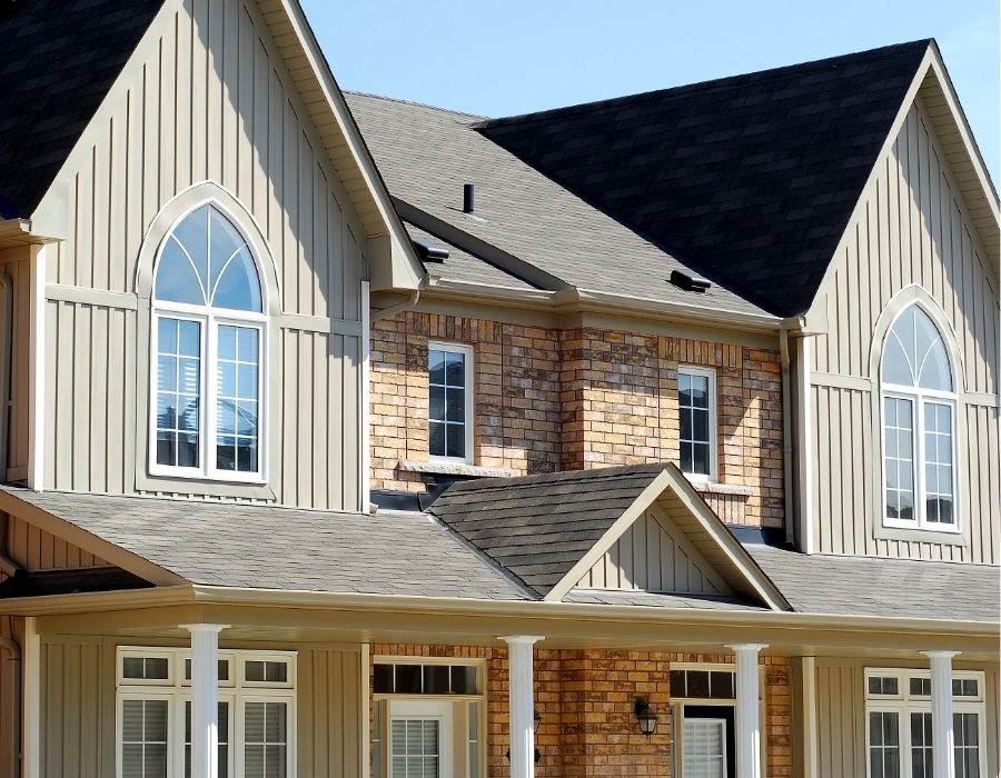 Custom two-story brick and siding home featuring arched windows, steep gable rooflines, and decorative columns, showcasing upscale residential architecture.