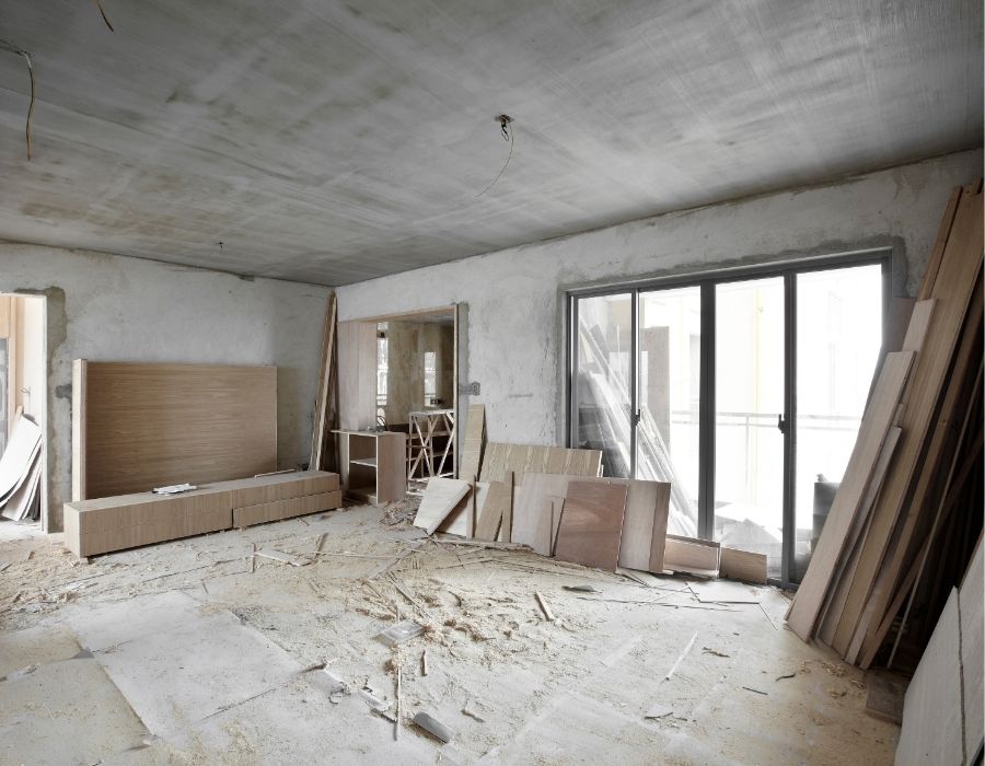 Interior home renovation in progress with unfinished drywall, construction materials, wood panels, and sliding glass doors in a residential remodeling project.