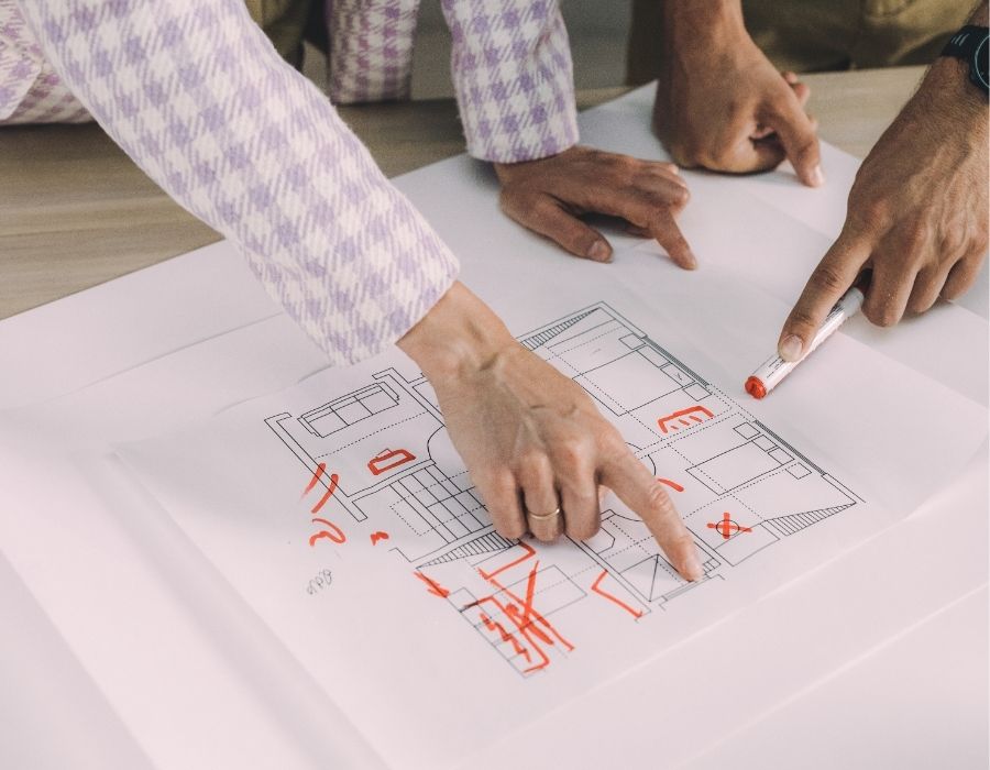 reviewing architectural floor plan with red construction markups, collaborating on residential design changes during project planning.