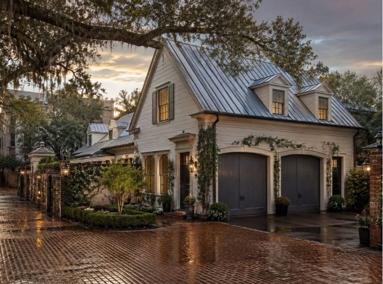 Luxury Savannah carriage house behind a historic Southern home, featuring Lowcountry architecture, brick lane access, live oak trees with Spanish moss, lantern-lit courtyard gardens, and a refined garage apartment with dormers and a standing seam metal roof at sunset after rain.